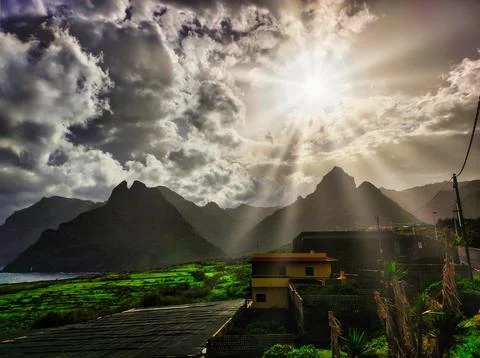 Sunlight breaks through clouds over mountains and buildings at the coast in.. Stock Photos