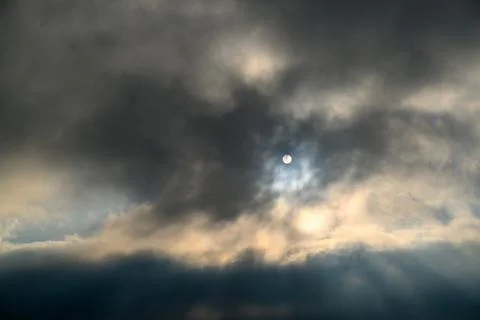 Sunlight breaks through dense clouds around a visible moon Stock Photos