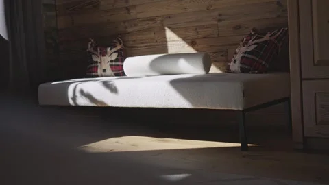 Sunlight casting moving shadows on a daybed in a rustic, wood paneled bedroom Stock-Footage 334649378