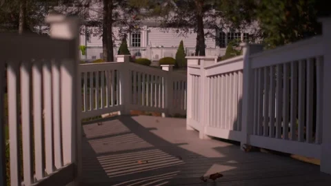 Sunlight casting shadows on a wooden deck with a white railing and house in Video stock 345260597