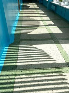 Sunlight casting striped shadows on a textured floor with green and gray tiles Фото