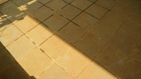 Sunlight casts diagonal shadow across beige tiled floor, creating warm geom.. Stock Photos