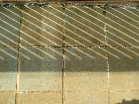 Sunlight casts diagonal striped shadows across weathered tiled floor with g.. Stock Photos