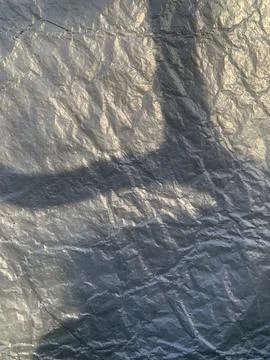 Sunlight casts intricate shadow patterns on a crumpled metallic surface in the Foto stock