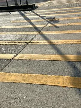 Sunlight casts long shadows across a worn pedestrian crossing with yellow s.. Stock Photos