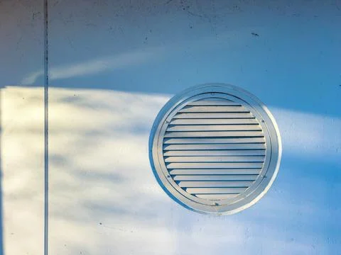 Sunlight casts shadows on a round vent on a wall in a quiet area during the.. Stock Photos