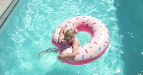 Sunlight causing child girl in swimsuit paddling pink donut float wearing Stock Footage 336784671