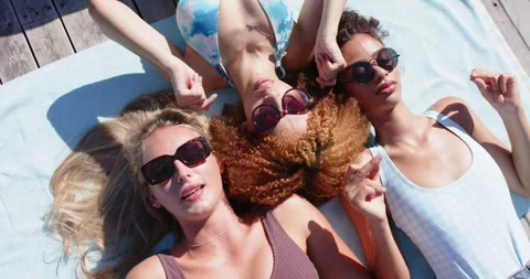 Sunlight causing three women on towel, center adjusting shades, left pointing, Stock Footage 339652379