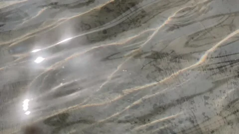 Sunlight caustic patterns reflecting on shallow water surface with gentle r.. Stock Footage 346659388