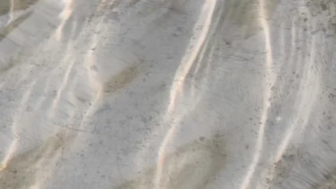 Sunlight caustic patterns shimmering on sandy riverbed, fluid water ripples.. Stockbeeldmateriaal 346659396