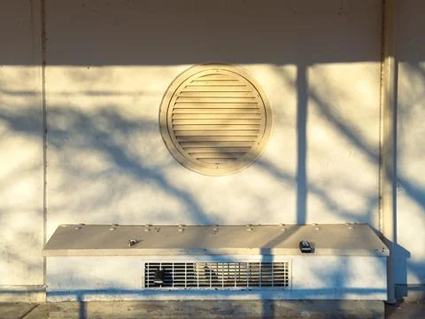 Sunlight creates long shadows on a wall with a round vent and a small ledge.  Stock Photos