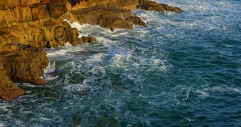 Sunlight drenches rugged cliffs of Cascais as turquoise waves churn foam below Stock Footage 309654725