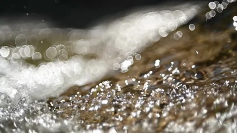Sunlight effects on water flowing over rocks in sunlight (slow motion, bokeh) Video stock 219641549