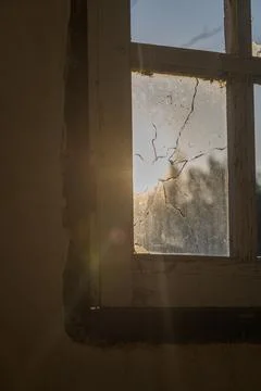 Sunlight filtering through a cracked window in an abandoned building at dusk Stock Photos