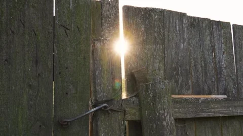 Sunlight filtering through a gap in old rustic wooden fence at sunset or sunrise Stock Footage 289531215