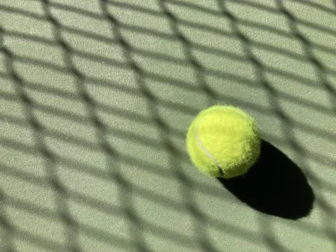 Sunlight filters through the net, casting shadow across a green tennis ball Stock-Fotos