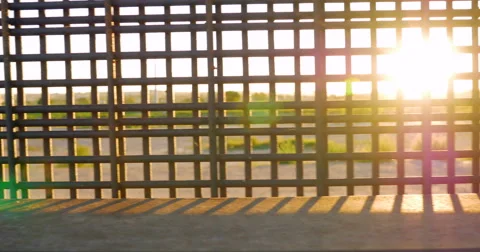 Sunlight Flickers Between the Bars of the Border Wall Dividing Countries 動画素材 67653245