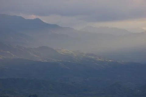 Sunlight getting through the clouds and mountains at sunset Stock Photos