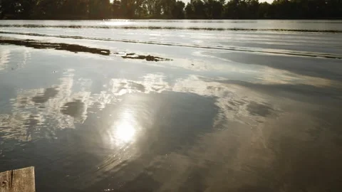 Sunlight glinting on rippling water with reflections of clouds and trees Stock Footage 337128467