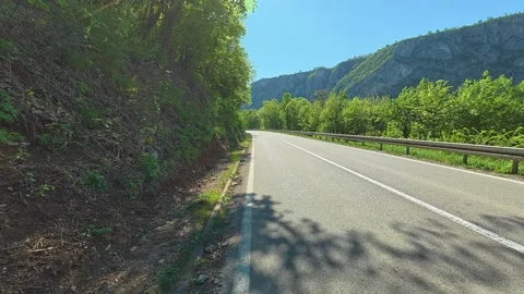 Sunlight glints off asphalt beside green hills. Balkan, Eastern Europe, POV Video stock 333349571