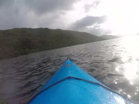 Sunlight glistens on the surface of this beautiful Scottish Loch and blue canoe Stock Footage 79884951