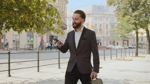 At sunlight handsome bearded man use phone walking on city street look around Stock Footage 140479428