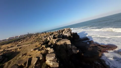 Sunlight highlights wave patterns splashing over dark stone formations Video stock 346076611