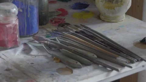 Sunlight hitting paintbrushes on a chaotic studio table full of paint Vídeos de archivo 147198451