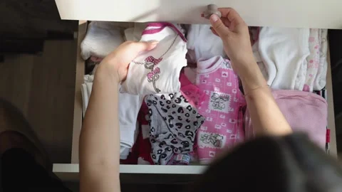 Sunlight illuminates a drawer full of baby clothes as a pregnant woman carefully 動画素材 326651331