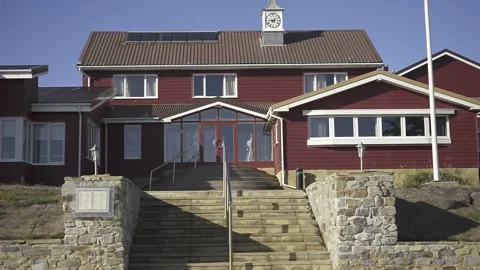 Sunlight illuminates a red building with a prominent clock and stone steps Stock Footage 293425767