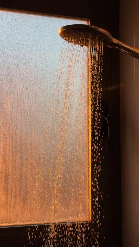 Sunlight illuminating shower with water falling against frosted glass window Stock Footage 295205647