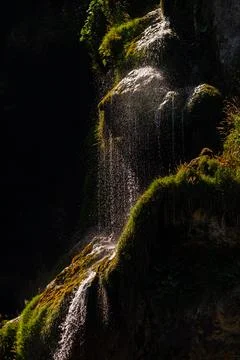Sunlight illuminating small waterfall stream flowing over mossy rocks in Pl.. Stock Photos