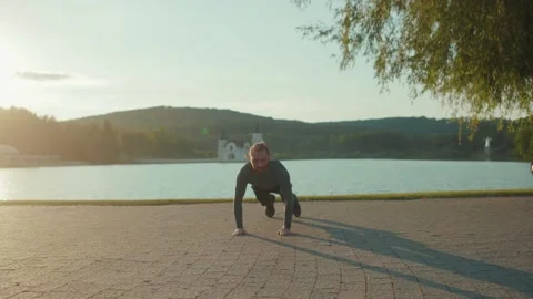 At sunlight man doing exercise near lake at outdoor workout sportswear active Stock Footage 138642159