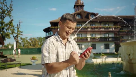 At sunlight man use of mobile phone at part near the fountain cellphone checking Stock Footage 116997275