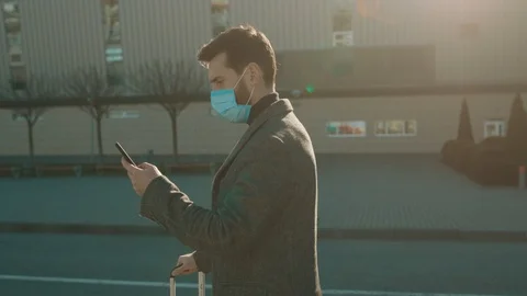 At sunlight man wearing Protective Face Mask use phone coughs hold suitcase Stock Footage 126619268
