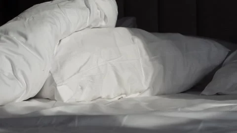 Sunlight moving across white bedding on a dark bed frame in a slow motion c.. Stock Footage 332578964