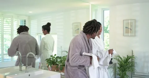 Sunlight nudging African couple getting ready in robes at double vanity sharing Stock Footage 336897695