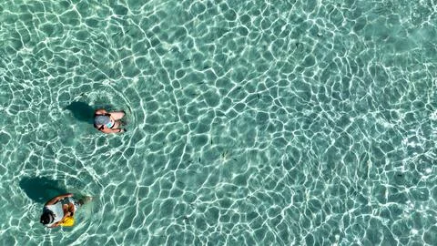 Sunlight paints dancing patterns across crystal clear shallows as two people Stock Photos