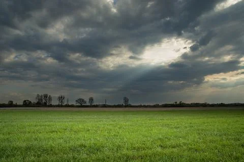 Sunlight passing through a hole in the clouds onto a green meadow Stock Photos