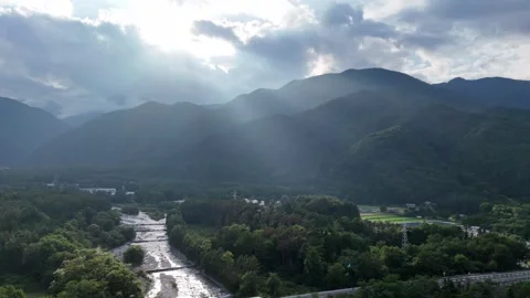 Sunlight pierces thick clouds above green mountains 動画素材 339871273