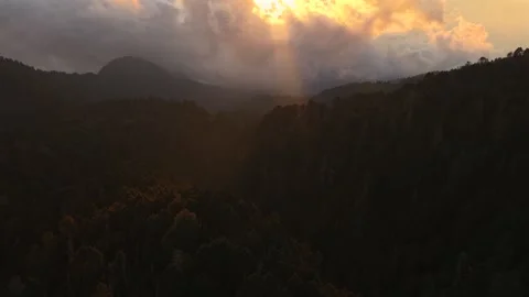 Sunlight piercing through dense clouds illuminating misty forested mountains Stock Footage 334137343