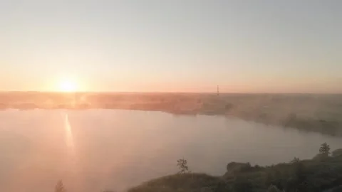 Sunlight is reflecting on a misty lake surrounded by trees and fields Stock Footage 293158809