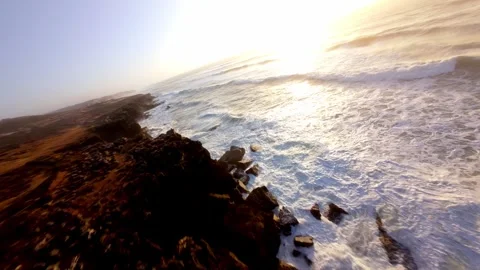Sunlight reflects on foamy waves hitting jagged cliffs 库存影片 346370540