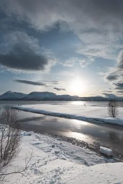Sunlight reflects on winding river flowing into Malangen fjord, Norway. Sno.. 스톡 사진