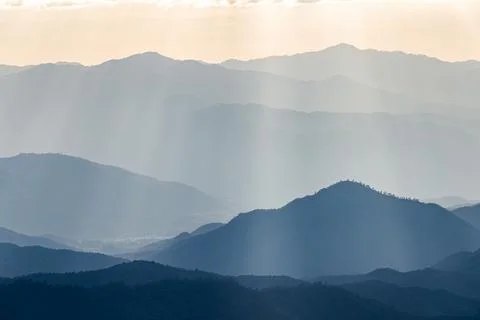 Sunlight shine through cloud onto blue mountain range. Stock Photos
