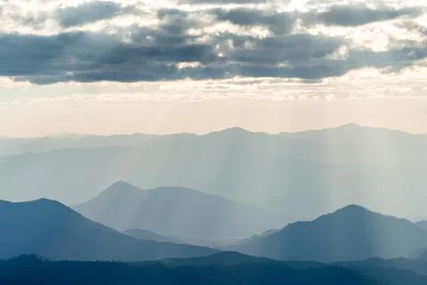 Sunlight shine through cloud onto blue mountain range. Stock Photos