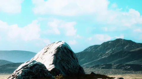 Sunlight shines on a large rock with mountains and blue sky in the background Stock Footage 344553685
