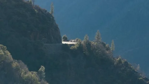 Sunlight shines on a paved mountain pass carved into steep forest terrain 動画素材 348020653