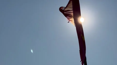 Sunlight shines through a tattered flag waving against a clear blue sky Stock Footage 345259795