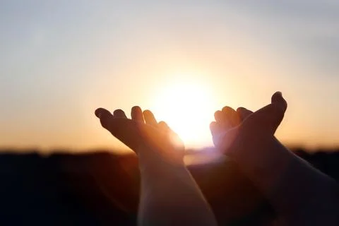 Sunlight shining through hands stretched out toward the sunrise Stockfoto's
